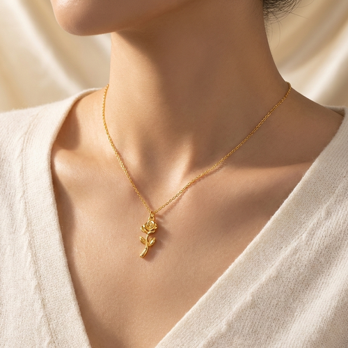 Gold necklace with a rose pendant worn by a person in a white outfit.